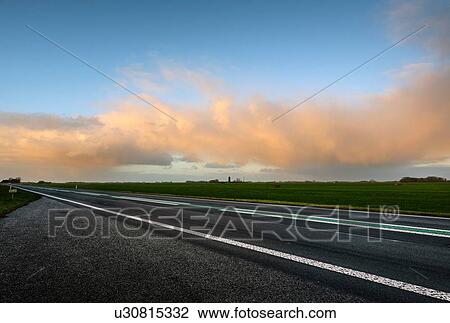 Stock Image - Rainclouds over rural road early on winter morning. Fotosearch