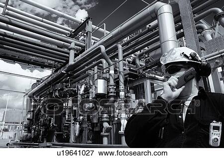 Stock Photo - Refinery worker talking into phone and standing in front of main fuel station inside refinery.. Fotosearch