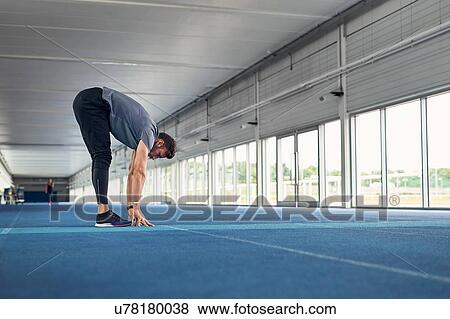 Stock Photo - Runner stretching on indoor running track. Fotosearch