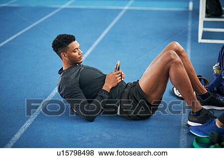 Runner texting while doing sit ups on indoor running track View Large Photo Image Stock Photo - Runner texting while doing sit ups on indoor running track. Fotosearch