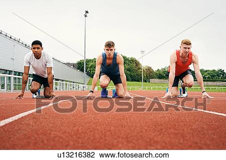Stock Image - Runners at starting line on running track. Fotosearch