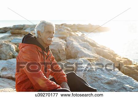 Stock Photo - Senior man watching sunset on beach, Livorno, Italy. Fotosearch