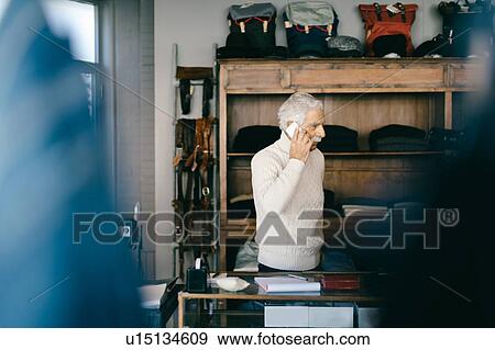 Stock Photo - Senior man working in clothes shop using mobile phone. Fotosearch