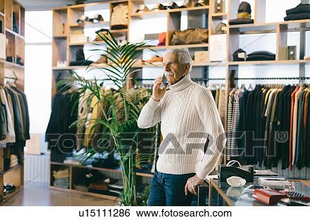 Stock Photograph - Senior man working in clothes shop using mobile phone. Fotosearch