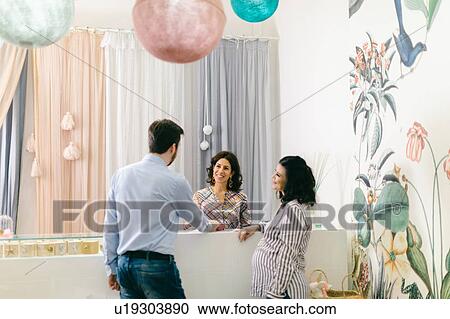 Stock Image - Shop keeper and pregnant couple at cash till. Fotosearch