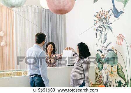 Stock Image - Shop keeper and pregnant couple at cash till. Fotosearch