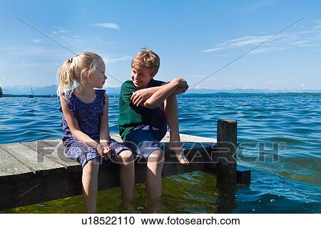 Stock Image - Siblings cooling feet in water, Lake Starnberg, Bavaria, Germany. Fotosearch
