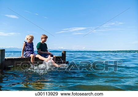 Stock Photo - Siblings cooling feet in water, Lake Starnberg, Bavaria, Germany. Fotosearch
