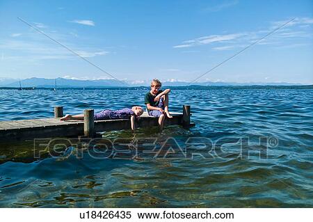 Stock Photography - Siblings relaxing on pier, Lake Starnberg, Bavaria, Germany. Fotosearch