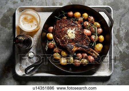 Stock Photograph - Skillet with large tomahawk steak & potatoes, overhead view. Fotosearch