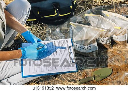 Stock Image - Soil Test. Female agronomist taking notes in the field.. Fotosearch