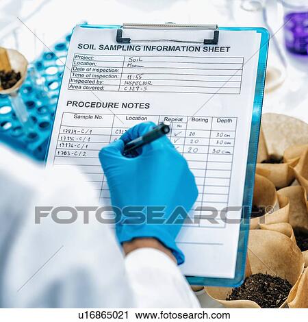 Stock Image - Soil testing laboratory. Close up image of female scientist wearing white coat taking notes in laboratory. Fotosearch