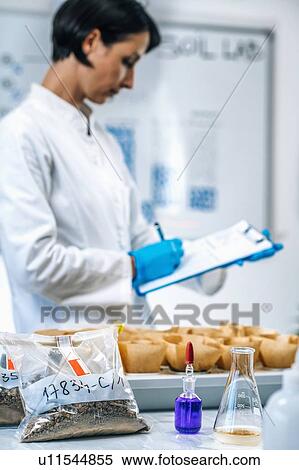 Stock Photography - Soil testing laboratory work. Close up image of female scientist wearing white coat taking notes in laboratory. Fotosearch