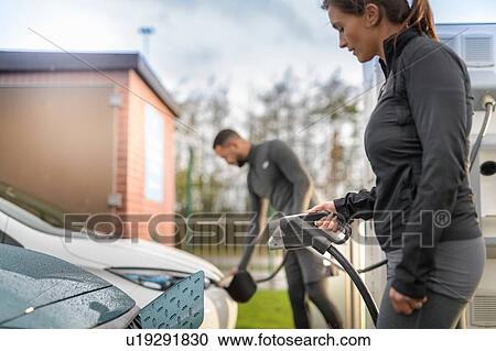 Stock Image - Sportsman and woman charging electric car at charging bay, Manchester, UK. Fotosearch