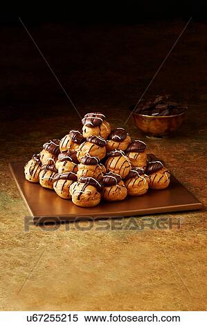 Stock Photography - Still life with stacked chocolate profiteroles on gold plate, christmas dessert. Fotosearch