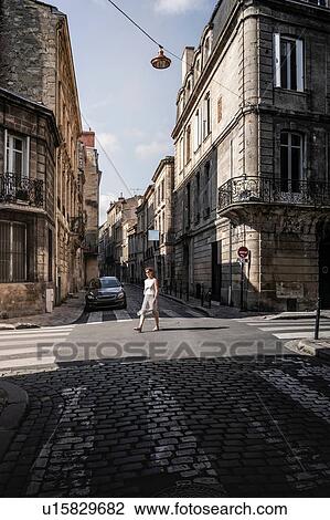 Stock Image - Street scene with woman crossing road, Bordeaux, Aquitaine, France. Fotosearch