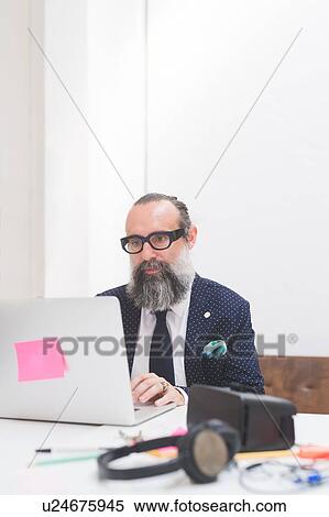 Stock Photography - Stylish businessman looking at laptop on office desk. Fotosearch