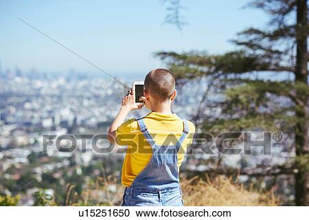 Stock Image - Teenage girl photographing view from cityscape hilltop, Los Angeles, California, USA. Fotosearch