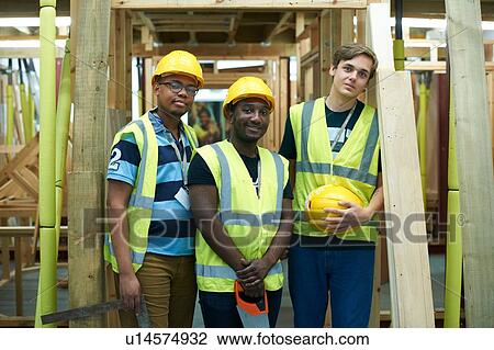 Stock Image - Three male higher education carpentry students in college workshop, portrait. Fotosearch