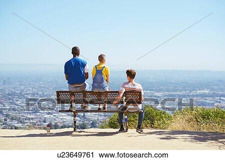 Stock Image - Three young adult friends on cityscape hilltop bench, rear view, Los Angeles, California, USA. Fotosearch