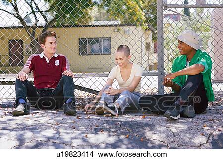 Picture - Three young adult friends sitting by park fence, Los Angeles, California, USA. Fotosearch