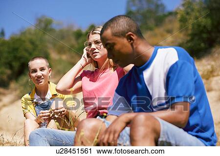 Stock Image - Three young adult friends sitting by dirt track, Los Angeles, California, USA. Fotosearch