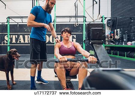 Stock Photo - Trainer guiding pregnant woman on rowing machine in gym. Fotosearch