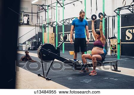 Trainer guiding pregnant woman using weights in gym View Large Photo Image Stock Photography - Trainer guiding pregnant woman using weights in gym. Fotosearch
