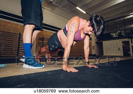 Stock Photo - Trainer standing over pregnant woman doing push ups in gym. Fotosearch