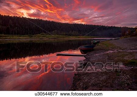 Stock Photo - Tree lined river with red orange sky, Ural, Sverdlovsk, Russia. Fotosearch