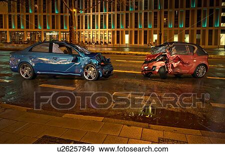Stock Photo - Two cars accident. Crashed cars on the road on city location at night time. A blue sedan against a red city car. Frontal collision with big damages.. Fotosearch