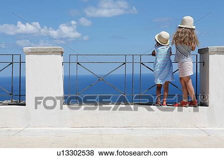 Two girls in sun hats looking out to sea from wall, Erice, Sicily, Italy View Large Photo Image Stock Photo - Two girls in sun hats looking out to sea from wall, Erice, Sicily, Italy. Fotosearch