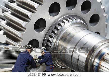 Stock Photo - Two industry workers with large gears and cogs.. Fotosearch