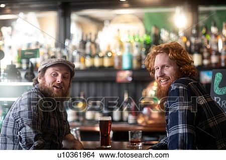 Two male customers looking over their shoulders from bar in traditional Irish public house View Large Photo Image Picture - Two male customers looking over their shoulders from bar in traditional Irish public house. Fotosearch