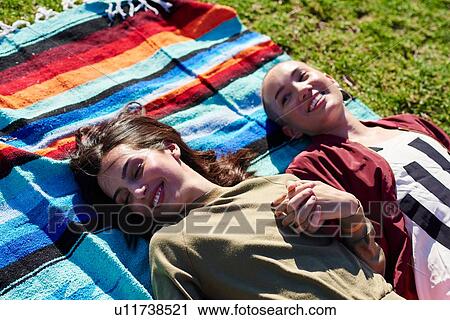 Stock Image - Two young female friends lying on picnic blanket in park, Los Angeles, California, USA. Fotosearch