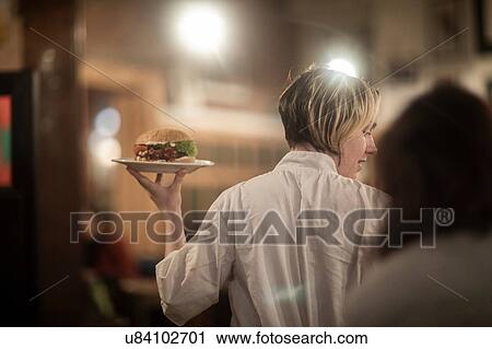 Waitress serving plate of burger in gastro pub View Large Photo Image Stock Image - Waitress serving plate of burger in gastro pub. Fotosearch