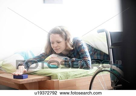 Stock Image - Wheelchair user in bed shutting off alarm clock. Fotosearch