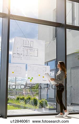Stock Image - Woman contemplating plans on glass wall. Fotosearch