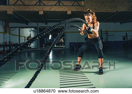 Stock Image - Woman exercising with battle ropes. Fotosearch