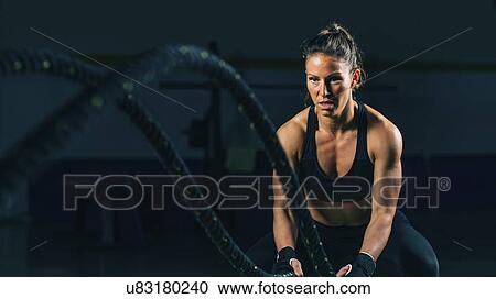 Stock Image - Woman exercising with battle ropes. Fotosearch