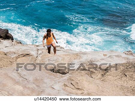 Stock Image - Woman exploring rocky coast, Spitting Caves, Oahu, Hawaii. Fotosearch