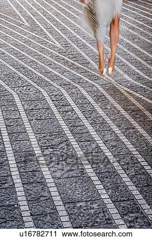 Stock Image - Woman in striped dress jumping mid air on stone pavement, cropped, Bordeaux, Aquitaine, France. Fotosearch