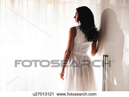 Stock Image - Woman in summer dress beside window. Fotosearch