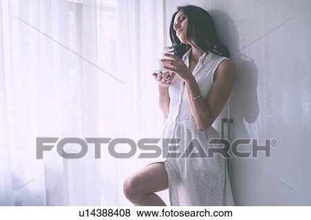 Stock Photo - Woman in summer dress beside window. Fotosearch