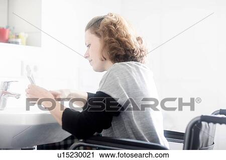 Stock Image - Woman in wheelchair at bathroom sink. Fotosearch