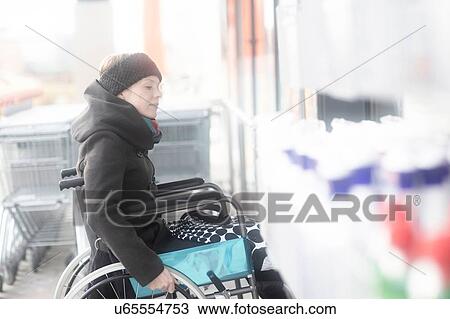 Stock Image - Woman in wheelchair going into supermarket. Fotosearch
