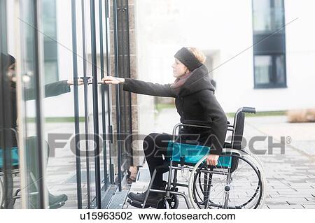 Stock Image - Woman in wheelchair opening door to building. Fotosearch