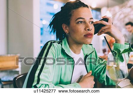 Stock Photo - Woman listening to message on mobile while having drink in bar. Fotosearch