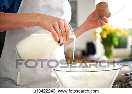 Stock Image - Woman pouring milk into mixing bowl in kitchen. Fotosearch