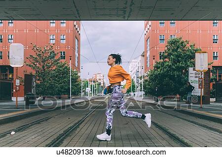 Stock Photo - Woman running across tram tracks, Milan, Italy. Fotosearch